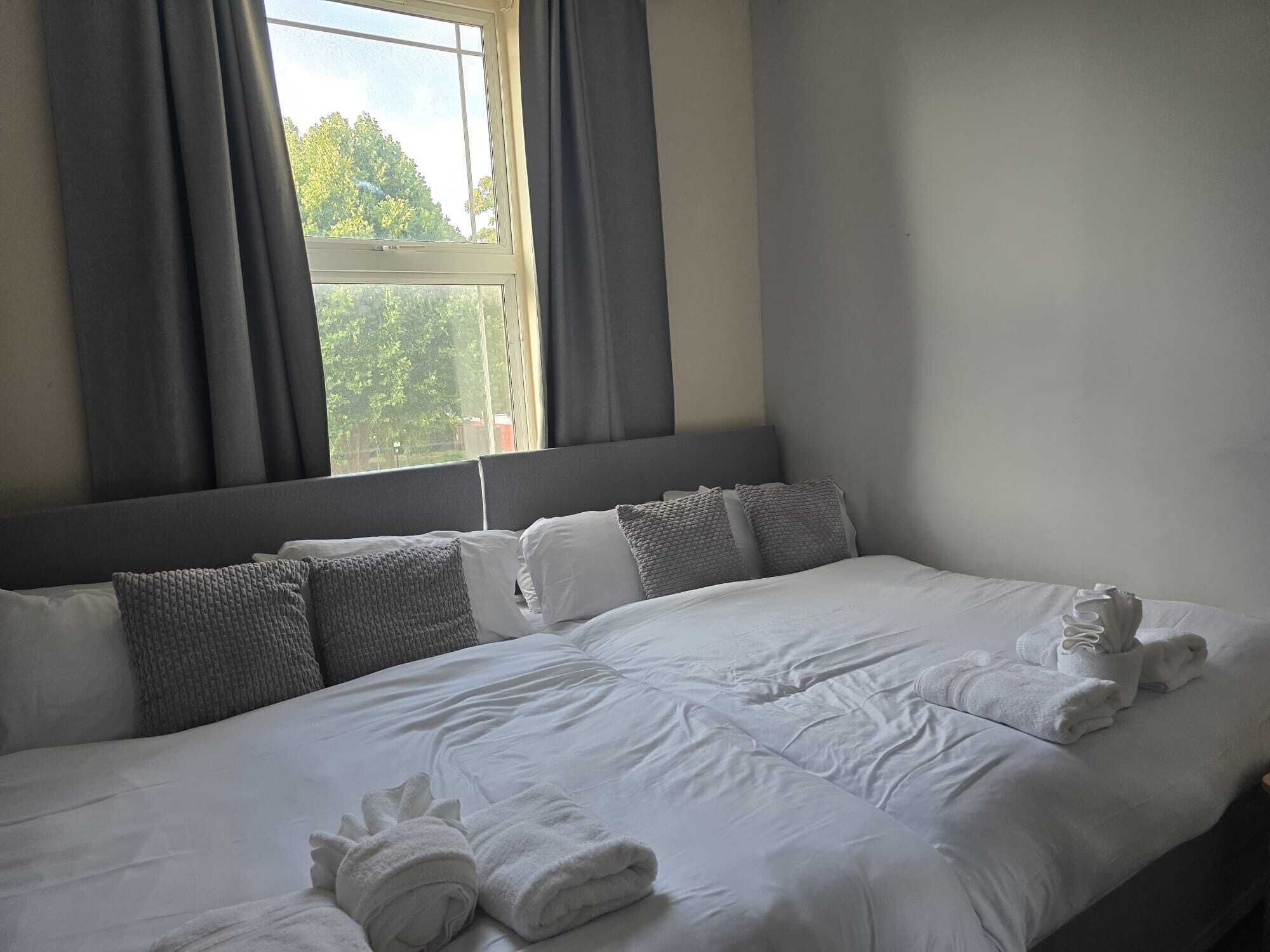 A hotel room with a bed, pillows, and a window with curtains.