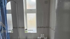 A small bathroom with a bathtub, a sink, a toilet, and a window. - Cosy Flat near Canary Wharf | Sleeps 6 (London)