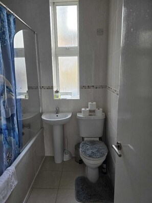 A small bathroom with a bathtub, a sink, a toilet, and a window. - Cosy Flat near Canary Wharf | Sleeps 6 (London)