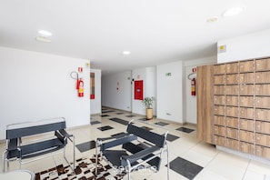Un vestíbulo con piso a cuadros, dos sillas de metal, un mueble de madera y una planta en maceta.