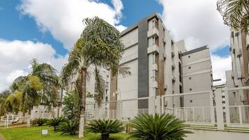Um edifício moderno com vários andares, grandes janelas e um jardim circundante com palmeiras.