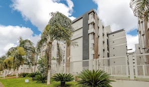 A modern building with multiple floors, large windows, and a surrounding garden with palm trees. - 1BR Apart With Self Check-in, Asa Sul Gdp0010 (Brasília)