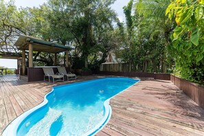 A swimming pool with a wooden deck, a covered seating area, and lush greenery. - Apartment on the Sand With Side sea View Jbm302 (Florianópolis)