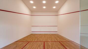Una cancha de squash con piso de madera y líneas divisorias rojas.