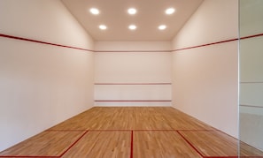 Una cancha de squash con piso de madera y líneas divisorias rojas.