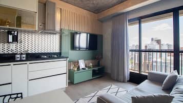 Un apartamento moderno con cocina, televisor de pantalla plana, sofá y un amplio ventanal con vista a la ciudad.