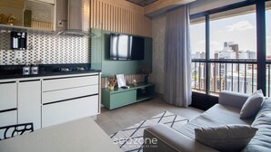 Un appartamento moderno con cucina, TV a schermo piatto, divano e un'ampia finestra vista città.