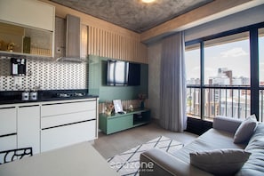 A modern apartment with a kitchen, a flat-screen TV, a sofa, and a large window with a city view. - Studio in a Condominium With a Pool Idvb2103 (Goiânia)