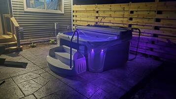 Jacuzzi exterior con escalones y una valla de madera al fondo.