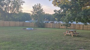 A backyard with a wooden fence, a picnic table, and a small tree.