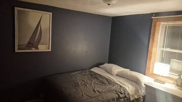 Un dormitorio pequeño con una cama individual, una lámpara de techo, una ventana con persianas y un cuadro en la pared.