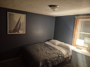 A small bedroom with a single bed, a ceiling light, a window with blinds, and a framed picture on the wall.