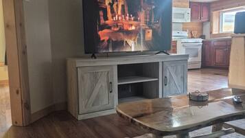 A living room with a television on a wooden stand, a coffee table, and a kitchen in the background.