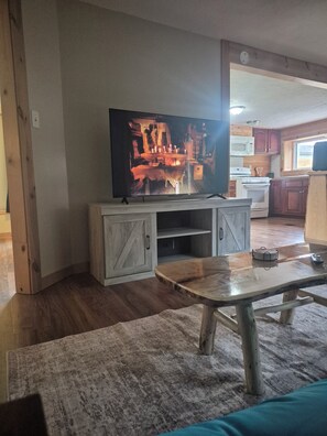Un salon avec un téléviseur posé sur un meuble en bois, une table basse et une cuisine en arrière-plan.