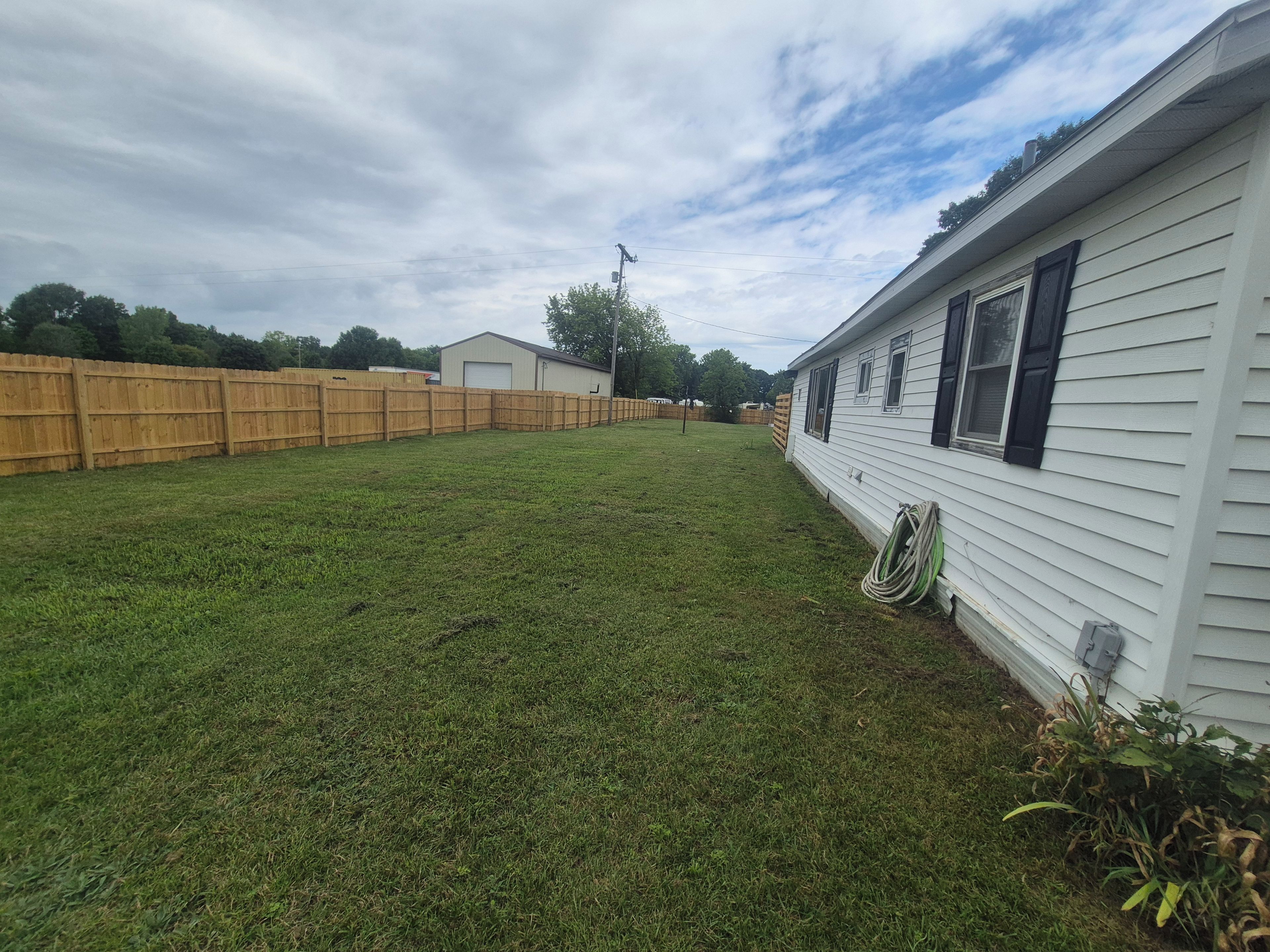 A residential area with a white house, a wooden fence, and a grassy yard.