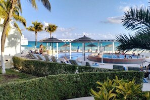 Uma área de piscina com espreguiçadeiras e guarda-sóis, rodeada por palmeiras e vista para o mar.