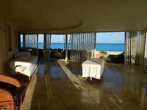 Quarto com uma grande porta de vidro deslizante que dá para uma varanda com vista para o oceano. Há duas camas e uma mesa pequena.