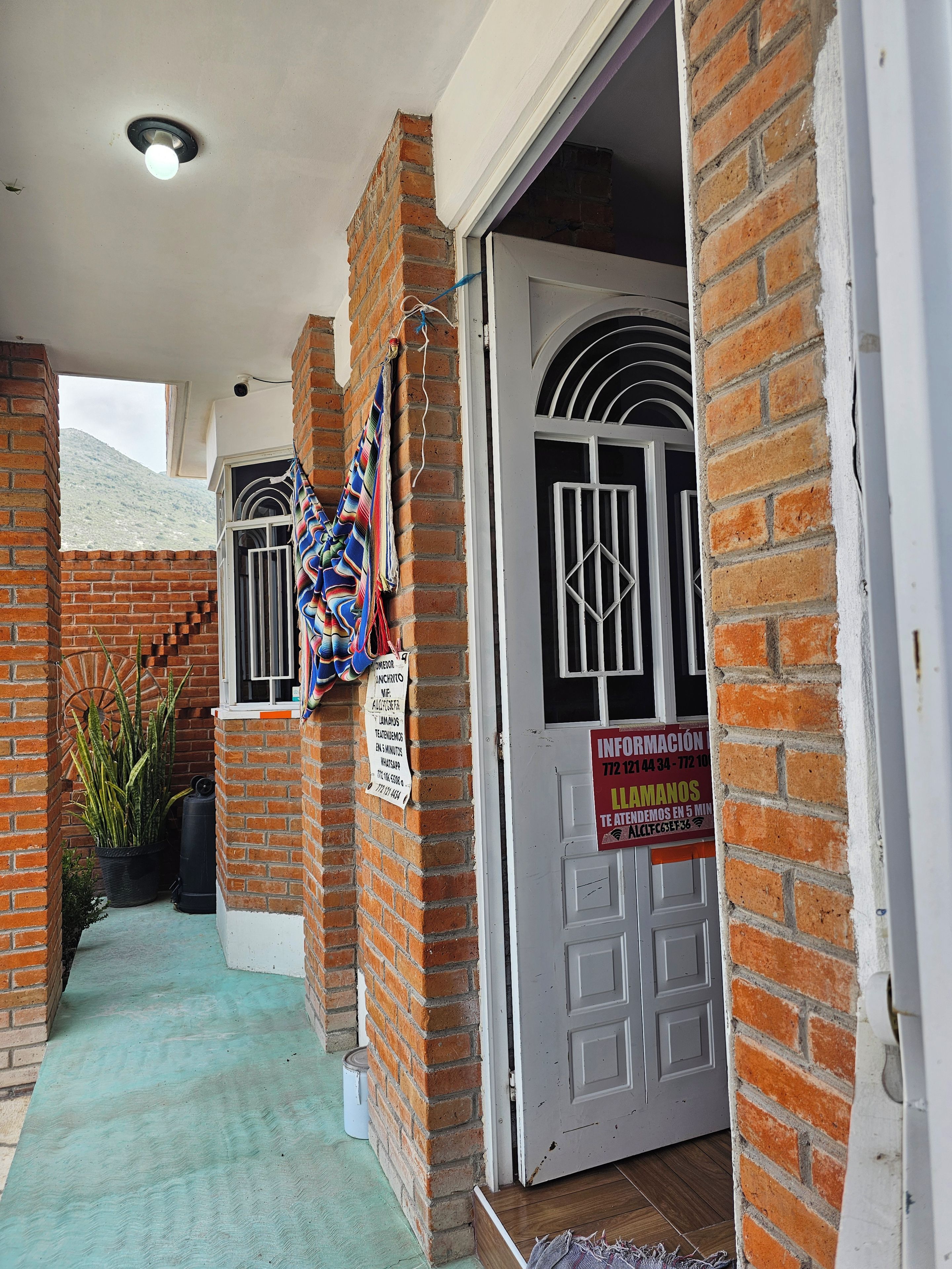 Fachada de tijolos com uma porta, uma janela com grades e uma placa.