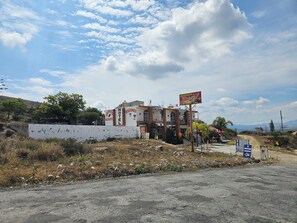 A hotel with multiple floors, a signboard advertising a restaurant, and a dirt road leading to it.