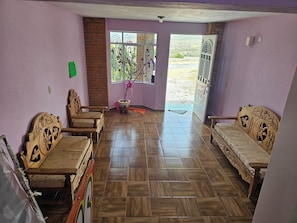Una habitación con piso de madera, dos sofás de madera, una mesa de madera y una ventana con vista al exterior.
