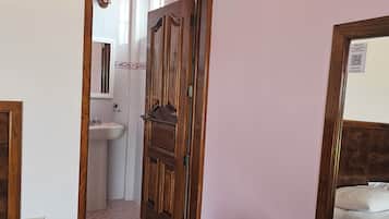 Una habitación con puerta de madera, un espejo, una cama y una mesita.