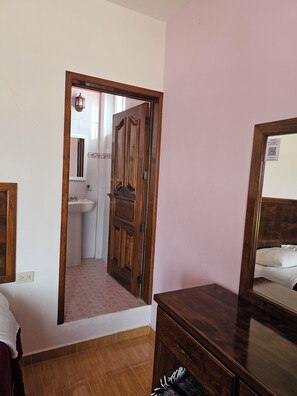 A room with a wooden door, a mirror, a bed, and a small table.