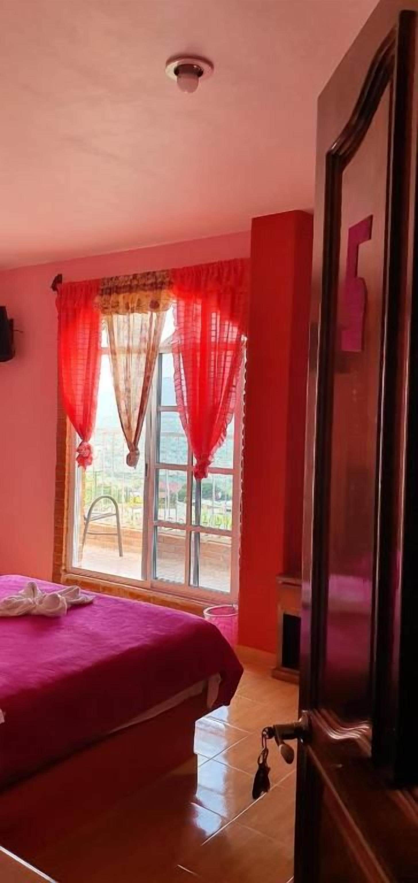 Um quarto com uma cama, uma janela com cortinas vermelhas e uma porta.