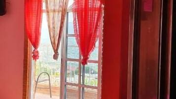 Um quarto com uma cama, uma janela com cortinas vermelhas e uma porta.