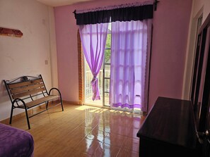 A room with a wooden bench, a small table, and a sliding glass door with purple curtains. - Hotel El Rancherito (Cardonal)