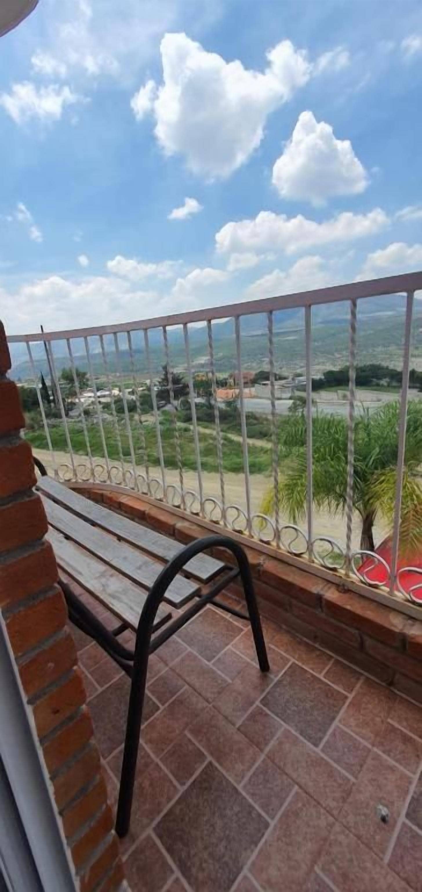 Een balkon met een metalen hekwerk, een houten bankje en uitzicht op een uitgestrekt landschap.