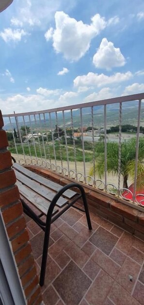 A balcony with a metal railing, a wooden bench, and a view of a distant landscape.