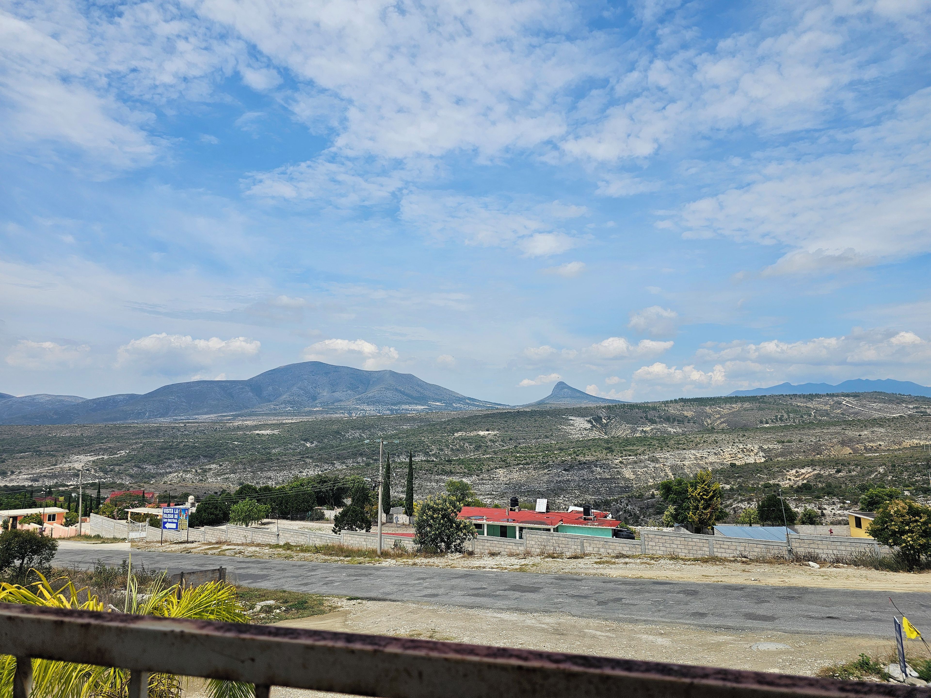 A landscape with a mountain range, a paved area with buildings, and a clear sky.