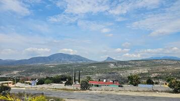 A landscape with a mountain range, a paved area with buildings, and a clear sky.