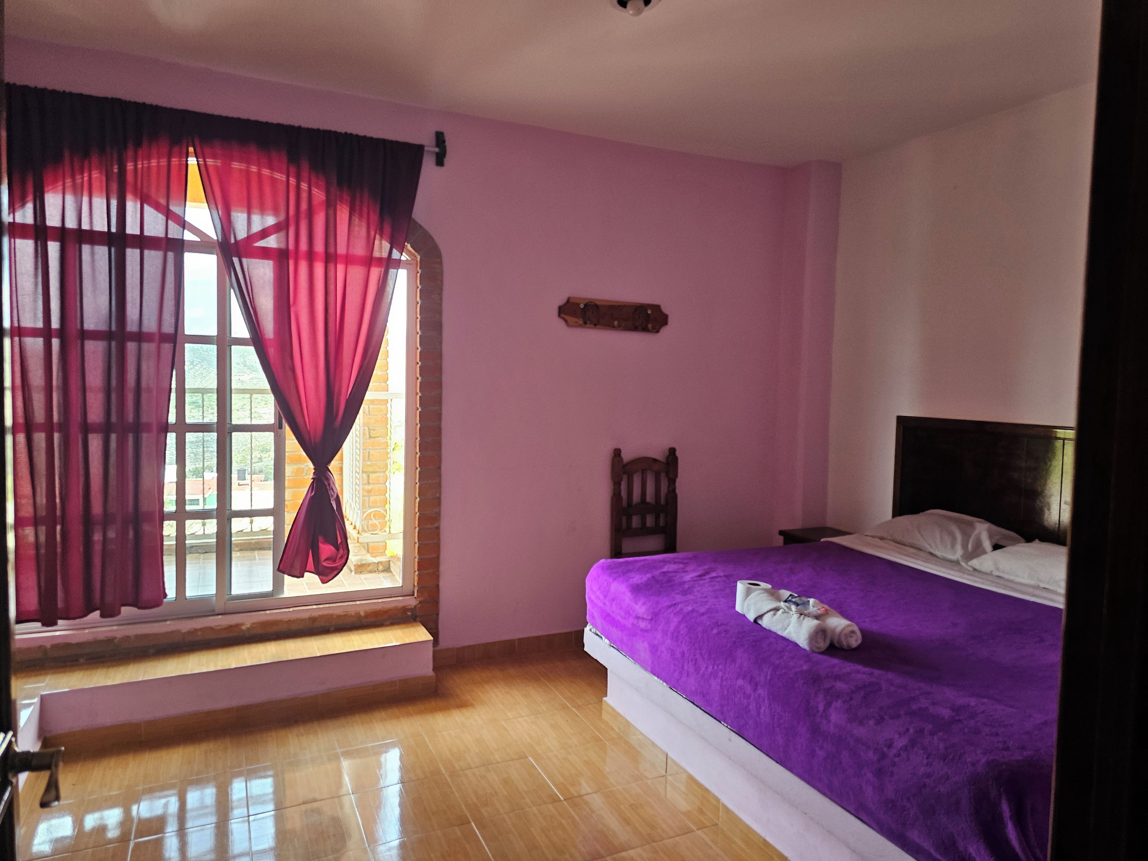 Een slaapkamer met een bed, een raam met gordijnen, een houten stoel en een hoofdeinde.
