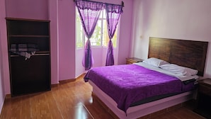 A bedroom with a bed, wooden headboard, a wardrobe, and a window with purple curtains.