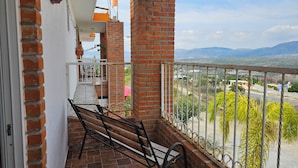 A balcony with a bench, brick walls, and a view of the landscape.