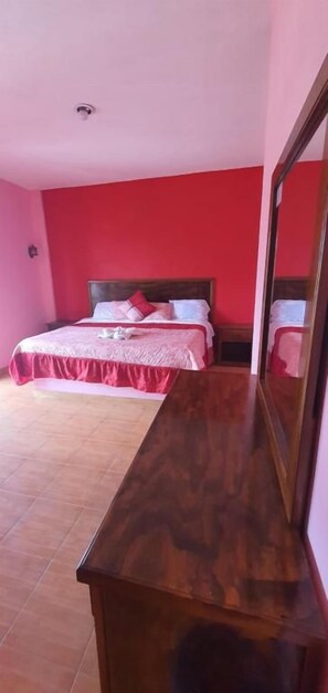 A bedroom with a bed, a wooden dresser, and a mirror.