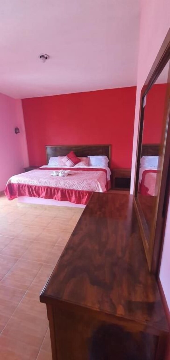 A bedroom with a bed, a wooden dresser, and a mirror.