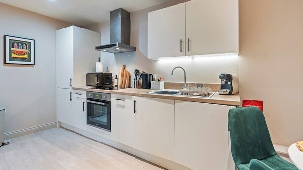 Een moderne keuken met witte kastjes, een inbouwoven, een magnetron en een koffiezetapparaat.