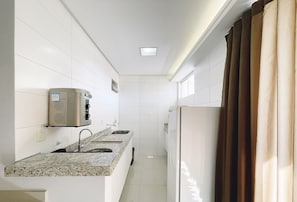 A narrow kitchen with white tiles, a granite countertop, a built-in microwave, and a window with brown curtains. - Flat in Setor Bueno 500m Vaca Brava Park Onx1410 (Goiânia)