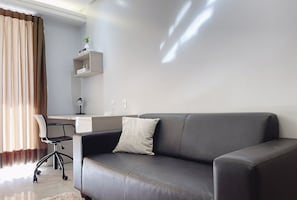 A modern living room with a grey sofa, a black office chair, and a desk with a computer. - Flat in Setor Bueno 500m Vaca Brava Park Onx1410 (Goiânia)