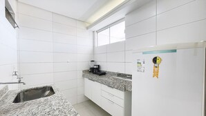Una cocina con azulejos blancos, un lavamanos, una encimera con cafetera y armarios.