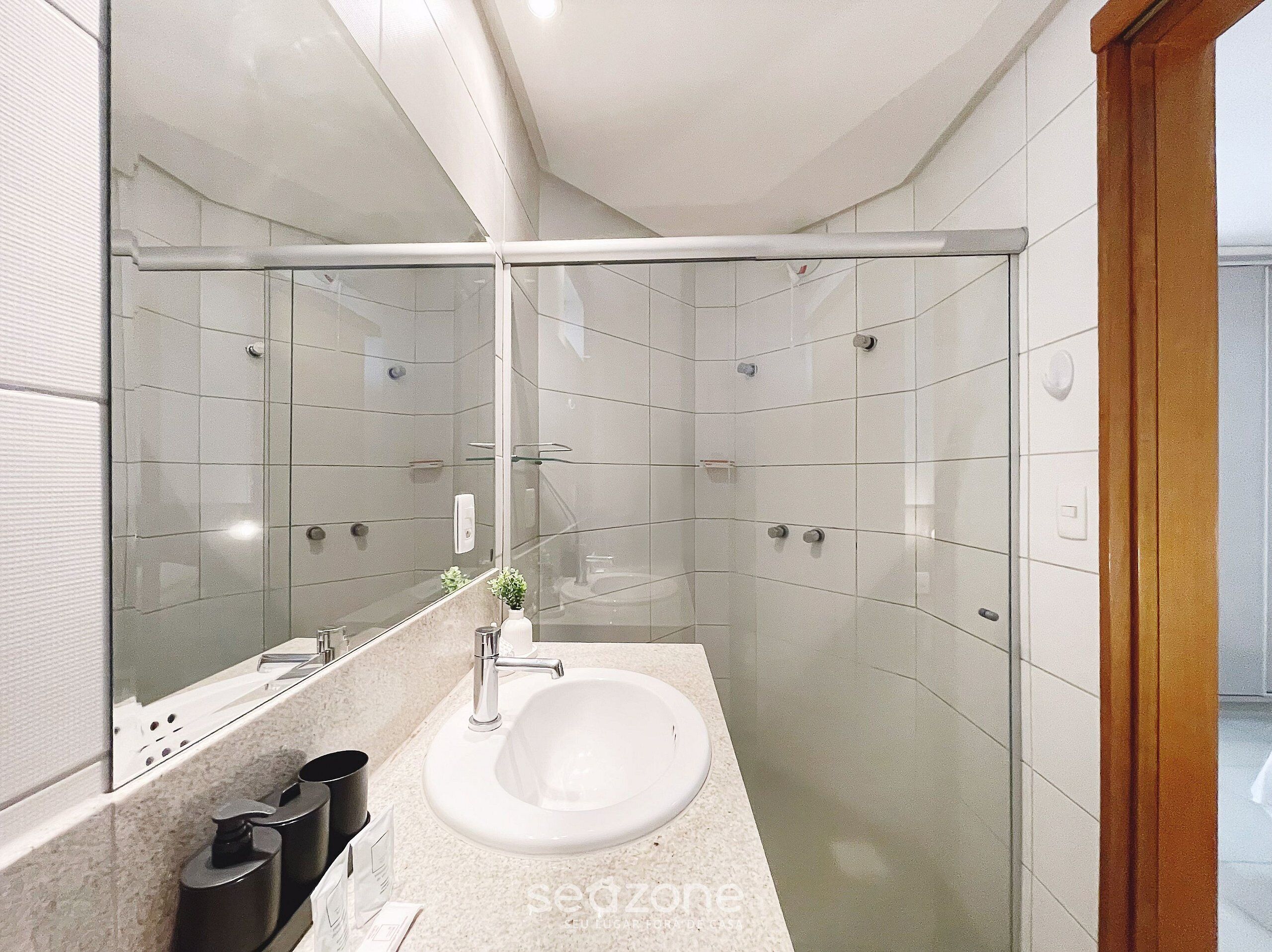 A modern bathroom with a glass shower enclosure, a white sink, and a large mirror.
