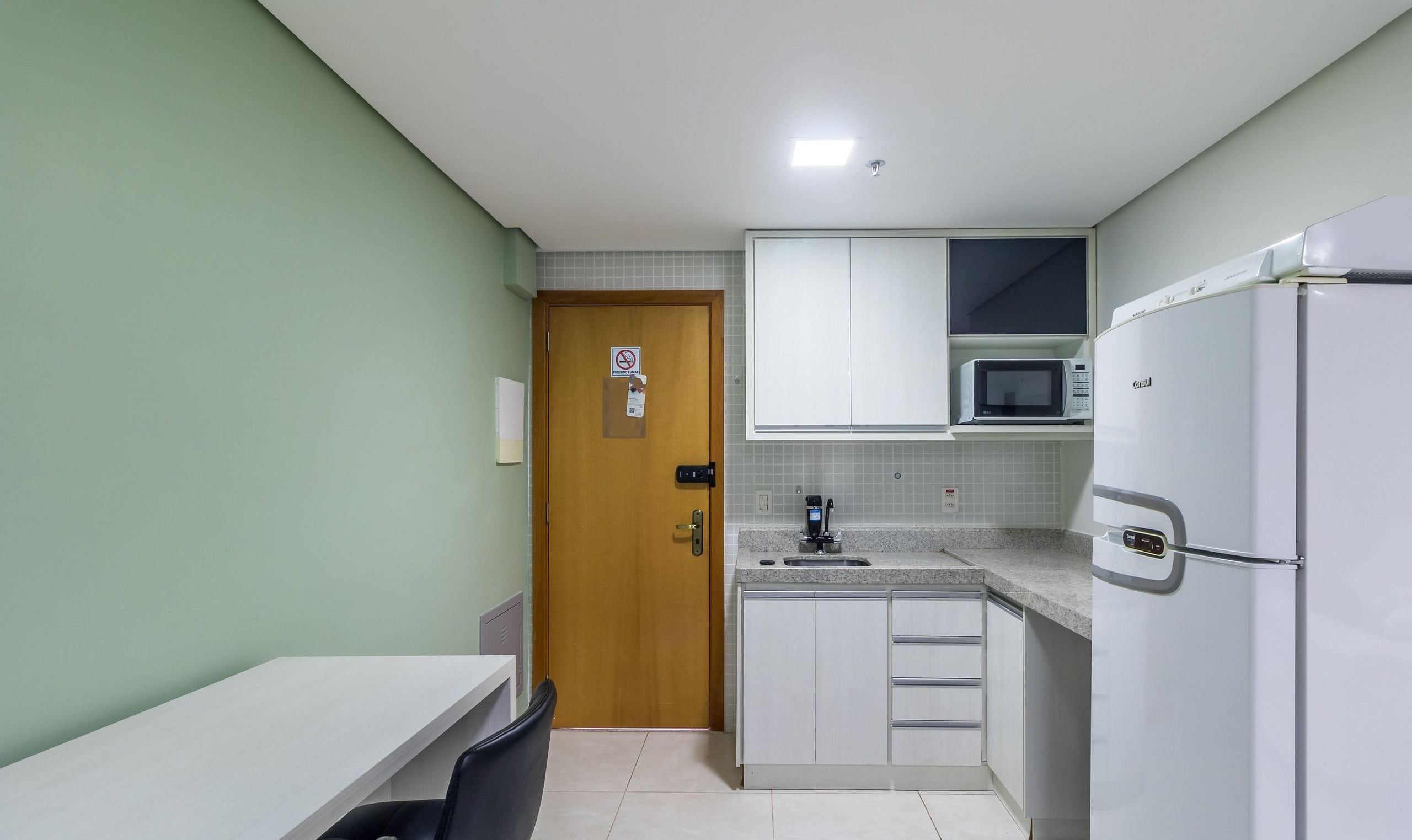 A compact kitchen with white cabinets, a microwave, a refrigerator, and a sink.