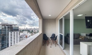 Ein Balkon mit zwei Stühlen, einem Sofa und einem Fernseher in einer modernen Wohnung mit Blick auf die Stadt.
