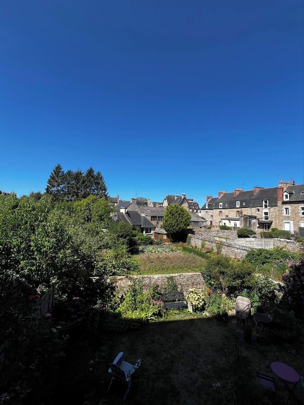 A residential area with stone buildings, a garden with various plants, and a clear blue sky.