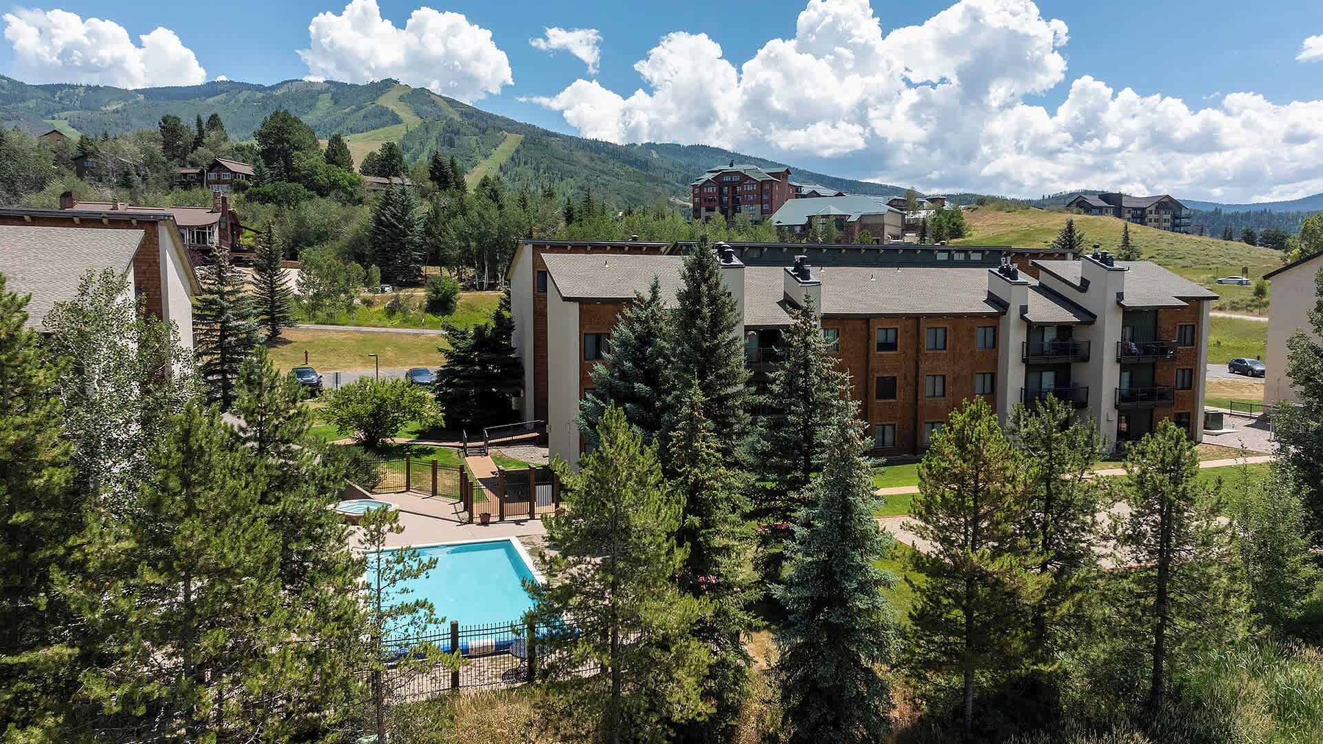 Un quartier résidentiel doté d’une piscine, entouré d’arbres et offrant une vue sur les montagnes.