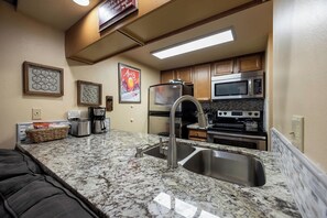 A compact kitchen with a granite countertop, stainless steel appliances, and wooden cabinets. - Lofted Mountain Lookout (Steamboat Springs)