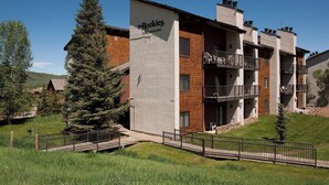 A multi-story building with balconies, a sign reading 'The Rockies Condominiums,' and a grassy area with a wooden deck. - Lofted Mountain Lookout (Steamboat Springs)