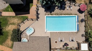 Ein Luftbild eines Hinterhofs mit einem rechteckigen Swimmingpool, einer Whirlpool-Einrichtung und einer Terrassenanlage mit Sitzgelegenheiten und Sonnenschirmen.